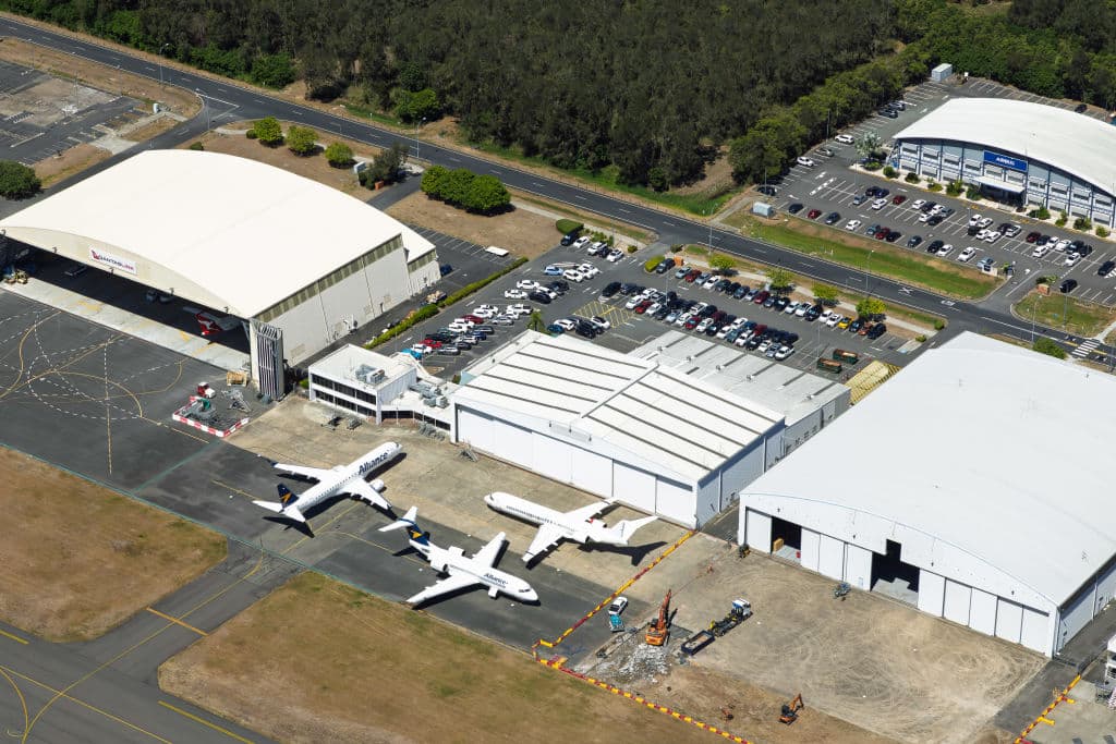An aerial shot of three aircraft sitting on the tarmac with three hangers pictured.