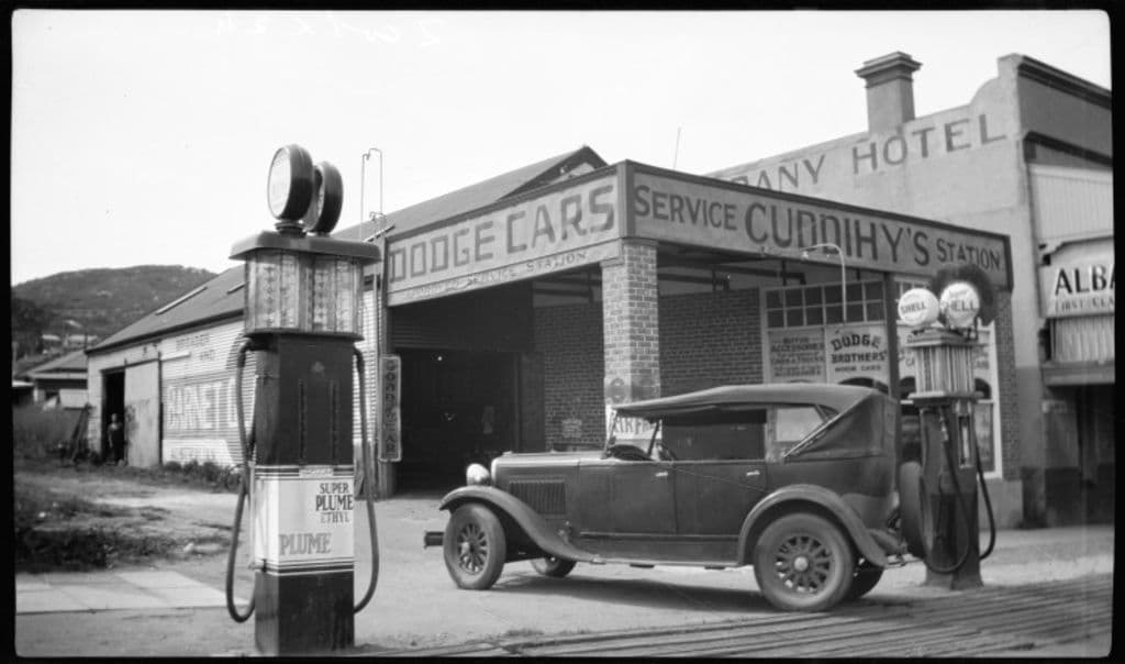 An old-fashioned car and petrol pump in a black and white photo.