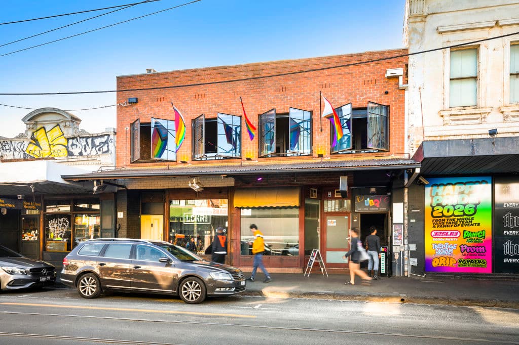 A red brick building features rainbow flags hanging from the top floor.