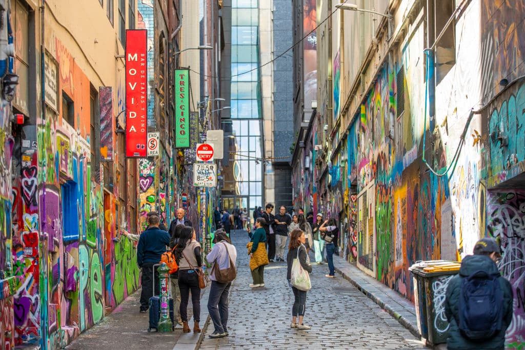 A laneway with people gathered on bluestones among walls covered in art and graffitti.