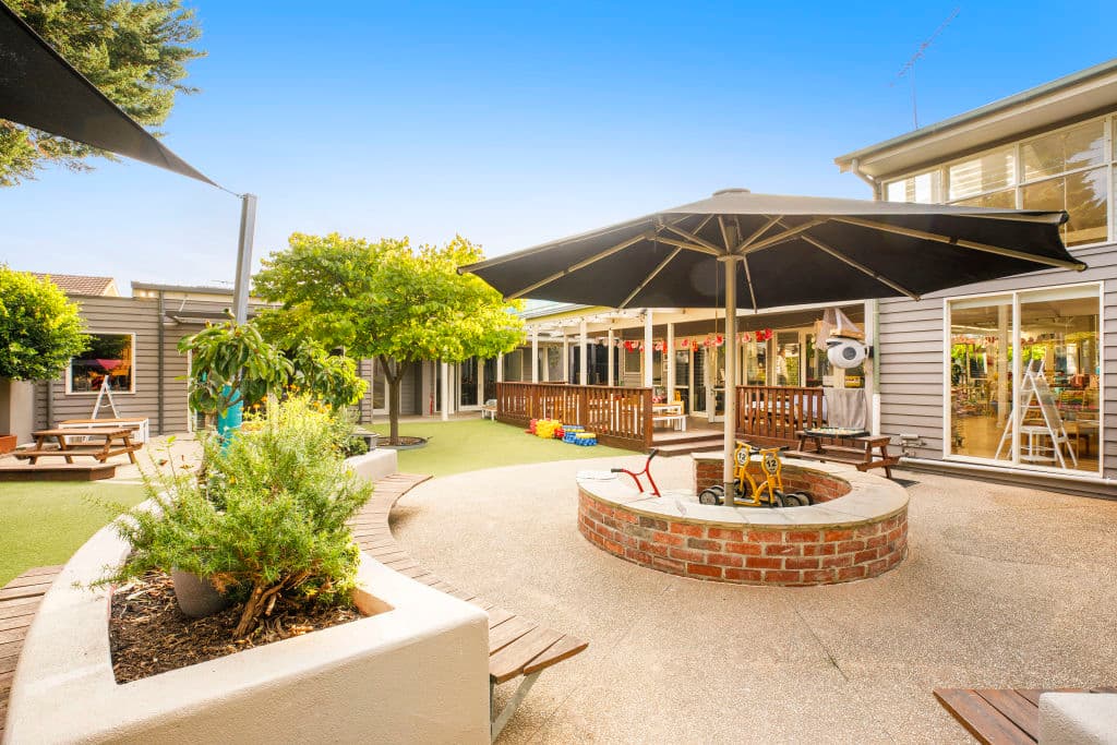 A paved outdoor area includes an umbrella to shade the children.