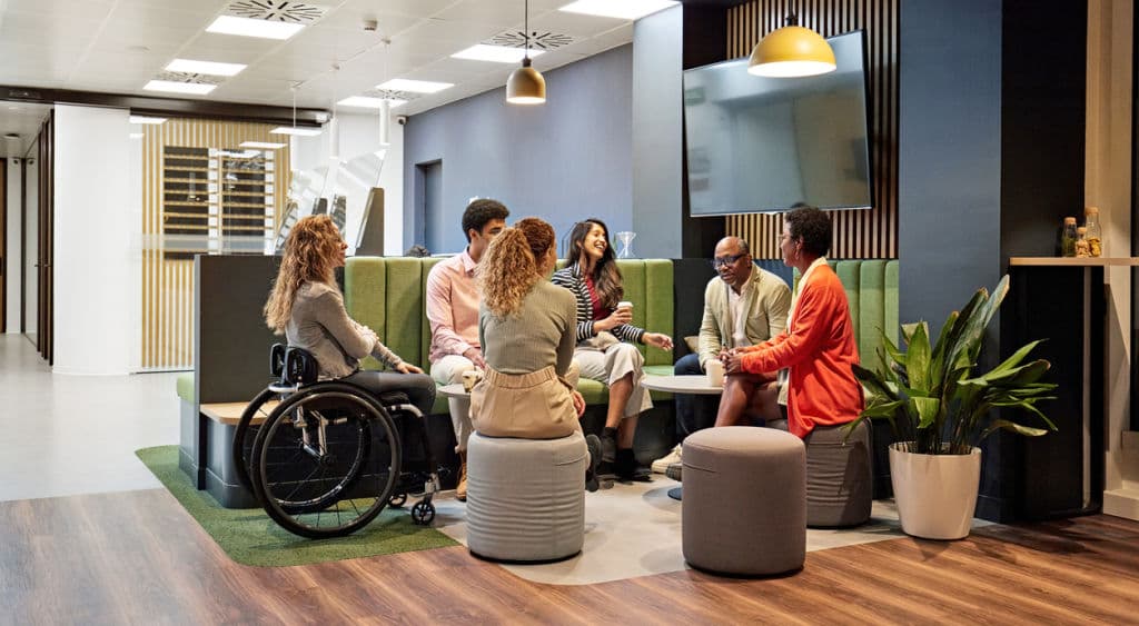 Full length view of relaxed group of colleagues in 20s, 40s, and 50s talking, sharing ideas, and laughing.
