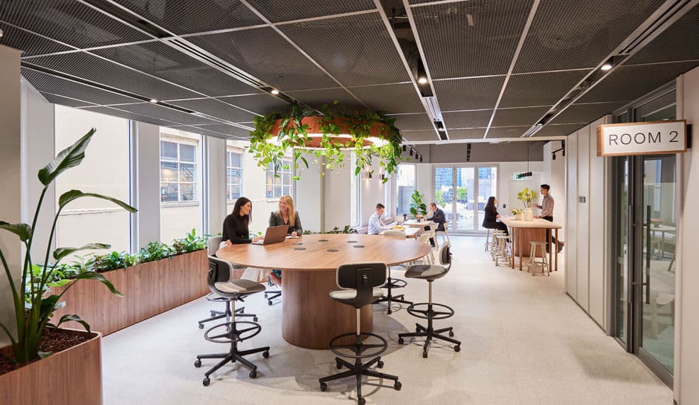 A render of two people standing at a round table in an office space.
