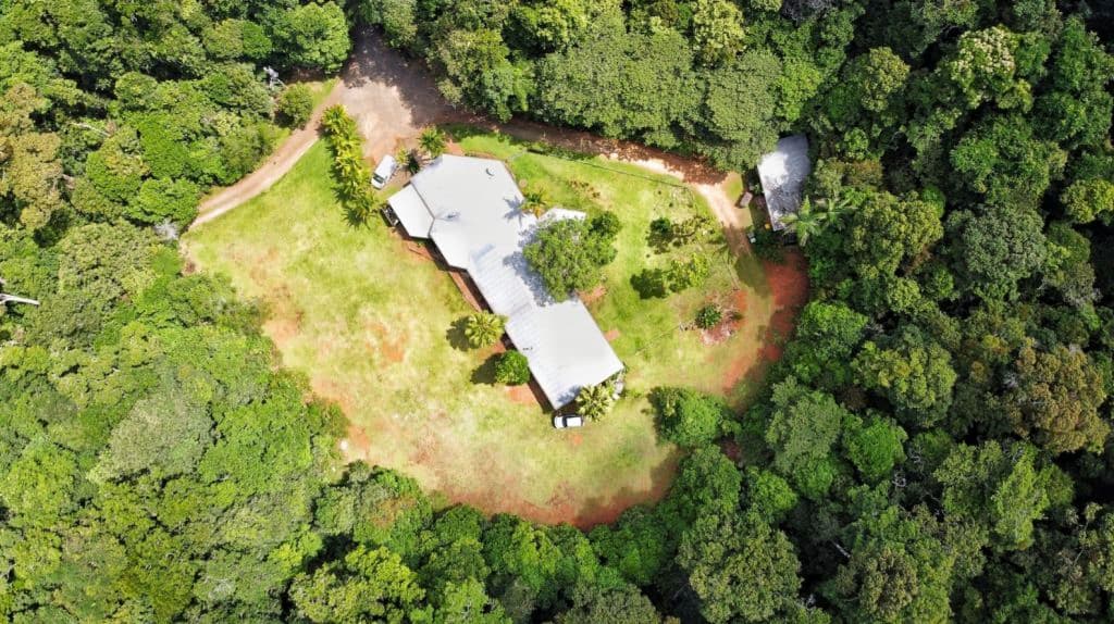 An aerial image of the owners residence which has a grass clearing, surrounded by rainforet.