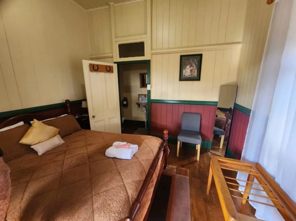 An inviting room with a large bed with warm natural tones throughout including a chocolate coloured bedspread, cream walls and a chair.