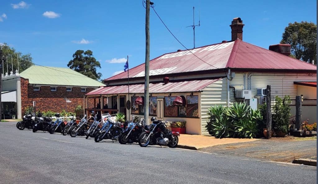 About 10 motorcyles are parked out the front of the pub on a sunny day.