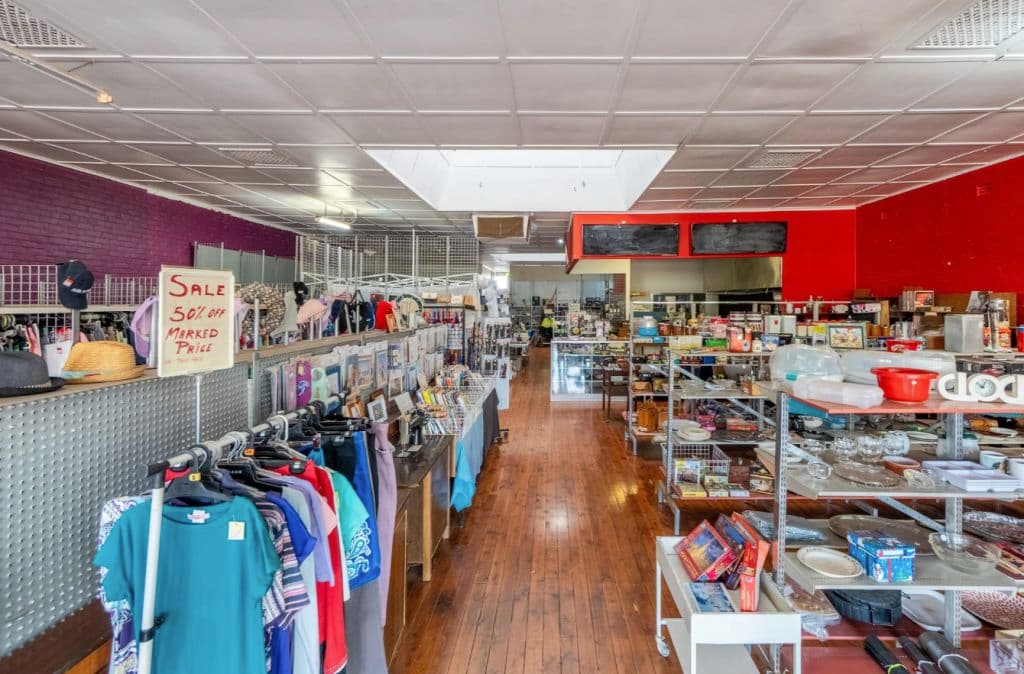 The op shop interior has rows of racks and shelves with goods displayed.