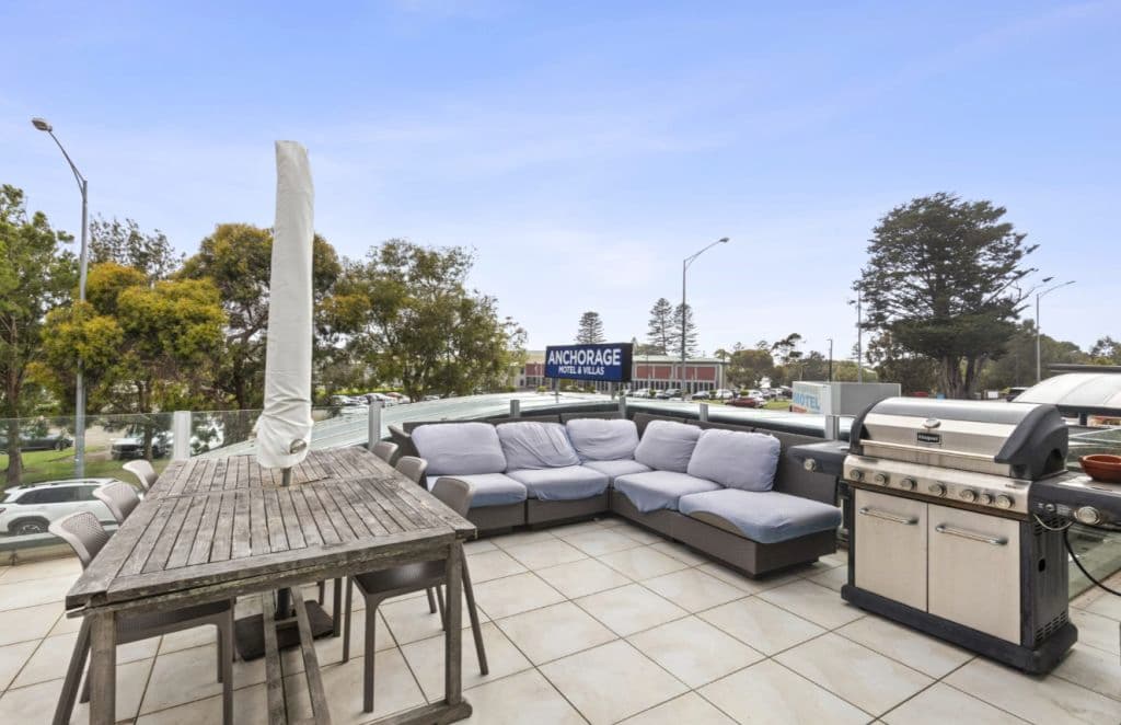 A view of a private balcony furnished with a grey outdoor couch and table with an umbrella.