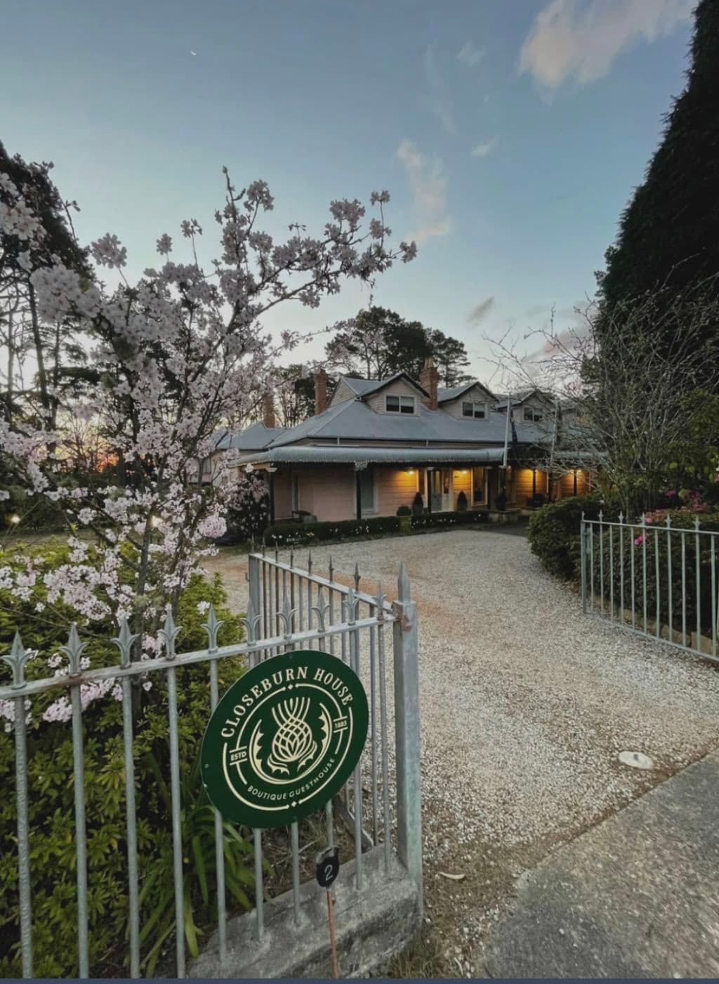 A gate opens up to a gravel driveway entrance to the weatherboard home.