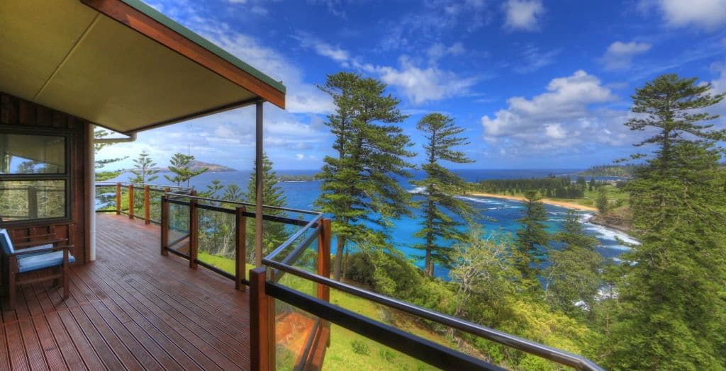 Views from a balcony to the ocean with pine trees dotting the skyline.