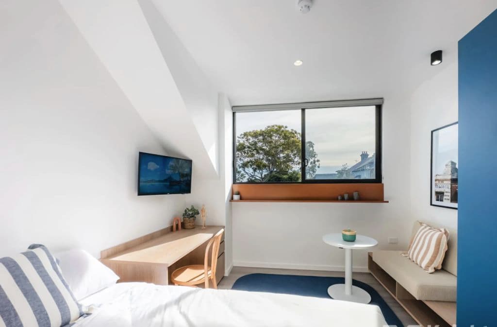 Inside a bedroom with a desk, table and brightly-lit window.