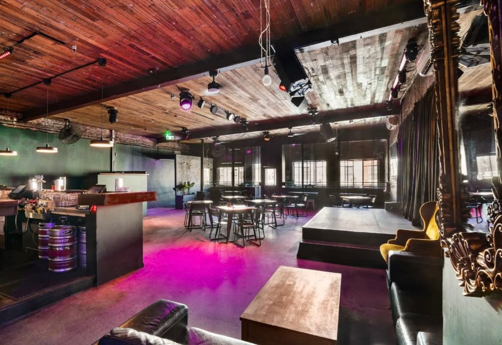 An upstairs space is lit up in a purple hue with timber furniture and ceiling throughout.