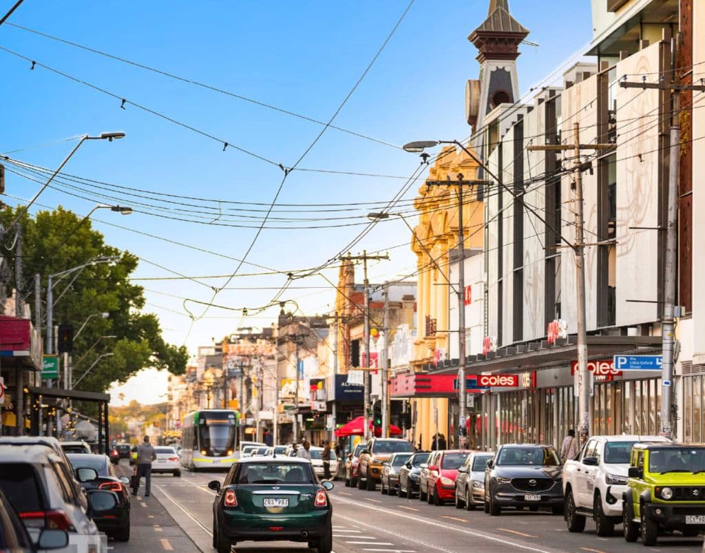 Trams and cars jostle for position along the busy strip where heritage buildings line the street.
