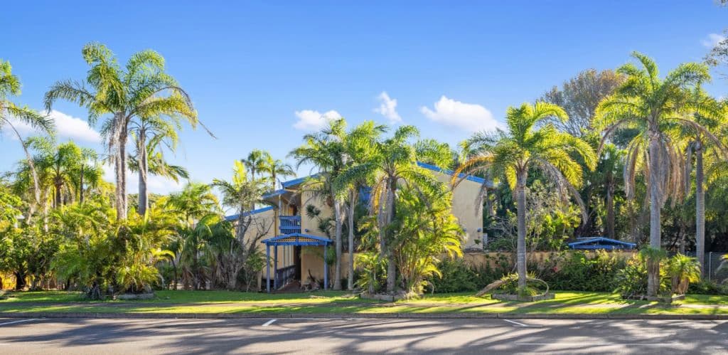 Palm trees dot the perrimetre of a block home to a cream and blue apartment complex.