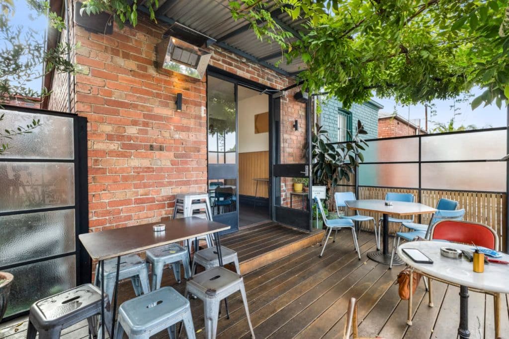 A timber deck with chairs and tables and a red brick wall of the building.