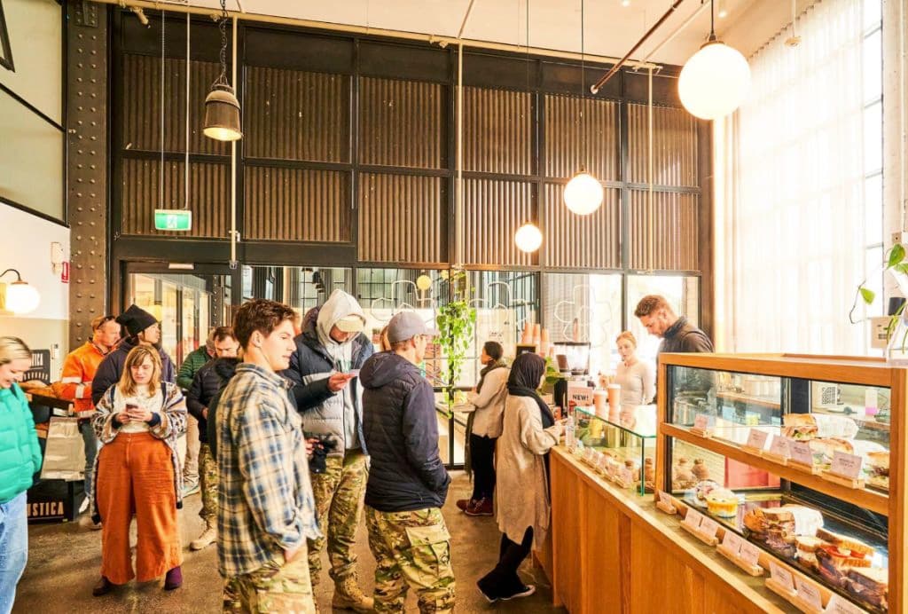 People line up in a cafe with goods on display.