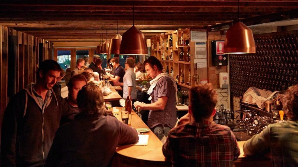 The packed bar shows bartenders making drinks and people lining the bar.