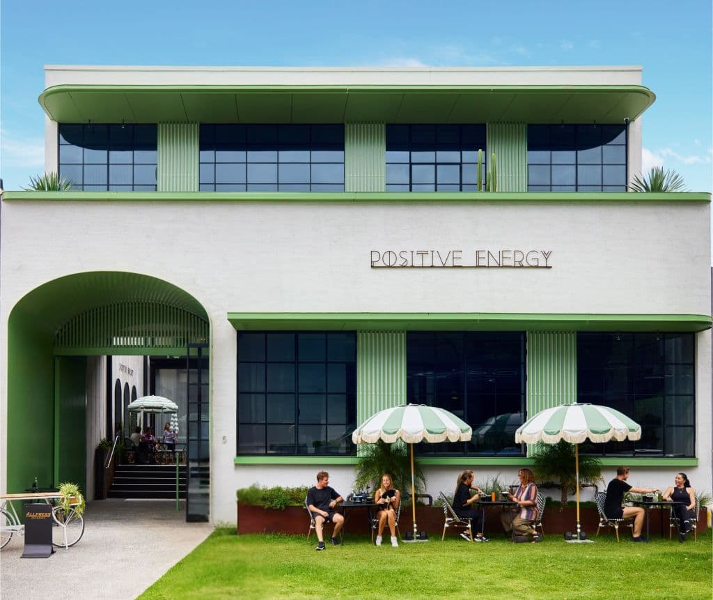 A lime green and white Palm Springs-style building with similar coloured umbrellas out the front with people sitting under
