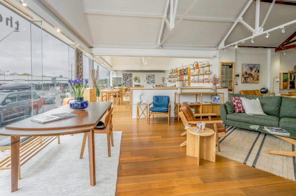 A brightly-lit space shows an open plan timber floor showroom with furniture throughout.