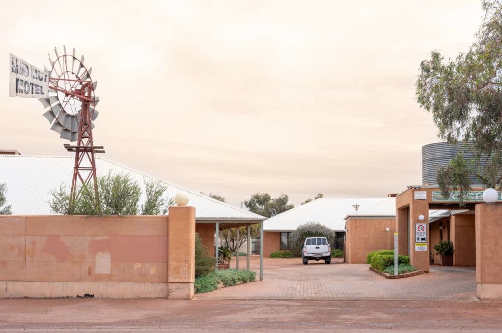The entrance to the Mud Hut Hotel has a high fence and windmill at the entry.
