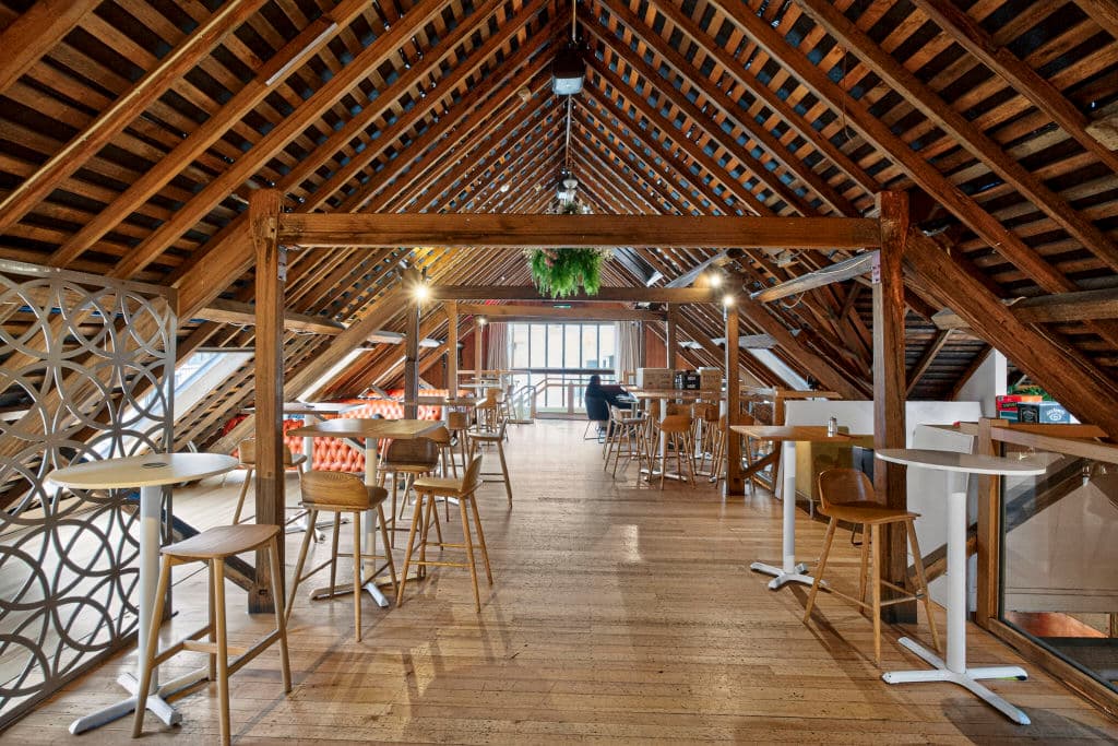 An A-frame roof with exposed beams and wooden floors with chairs and tables.