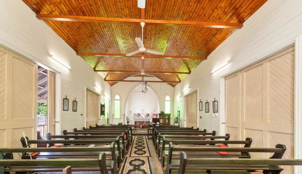 Inside a church building with a timber ceiling, pews and fans.