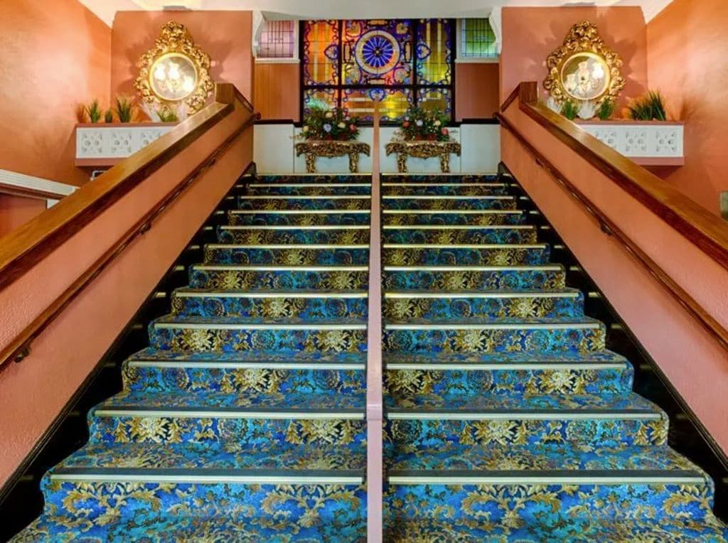A blue and gold carpeted staircase with salmon coloured sides and gold touches.