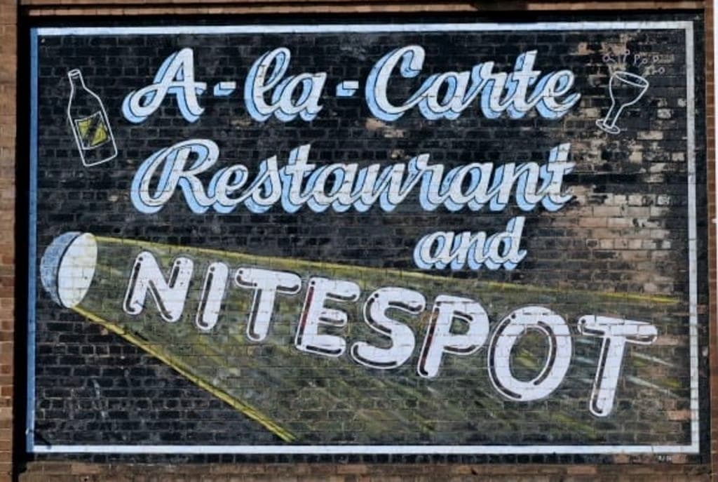 A street art depiction of the theatre's use as a restaurant and night spot are seen on the brick wall.