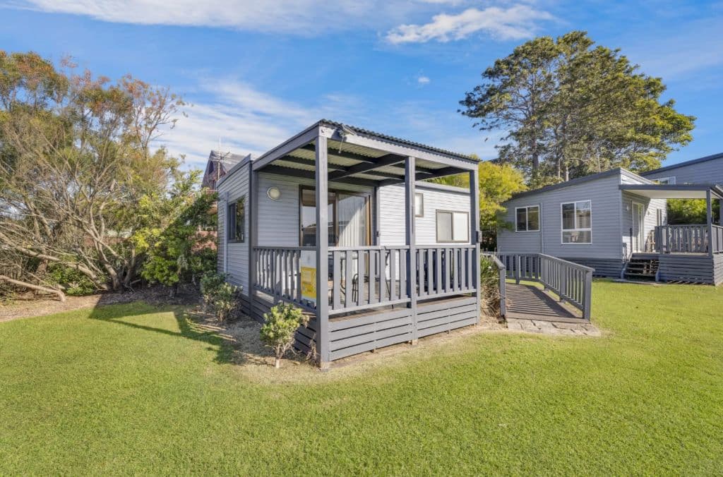 A cute cabin painted in grey tones upon a grass surface.