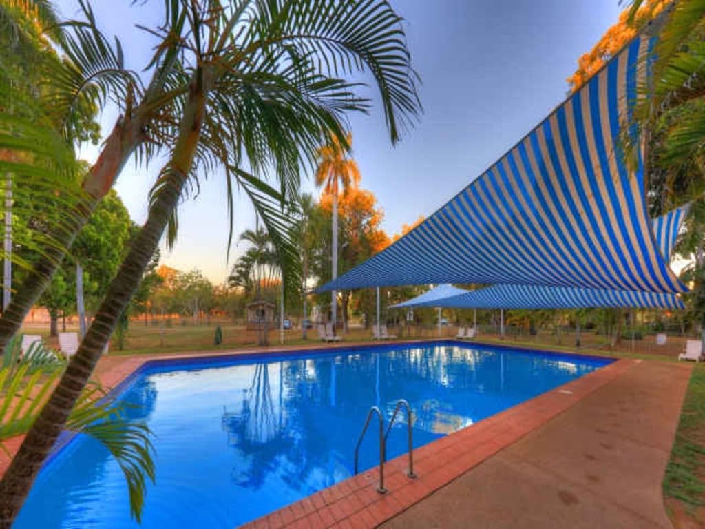A pool with palm trees and a shade sail.