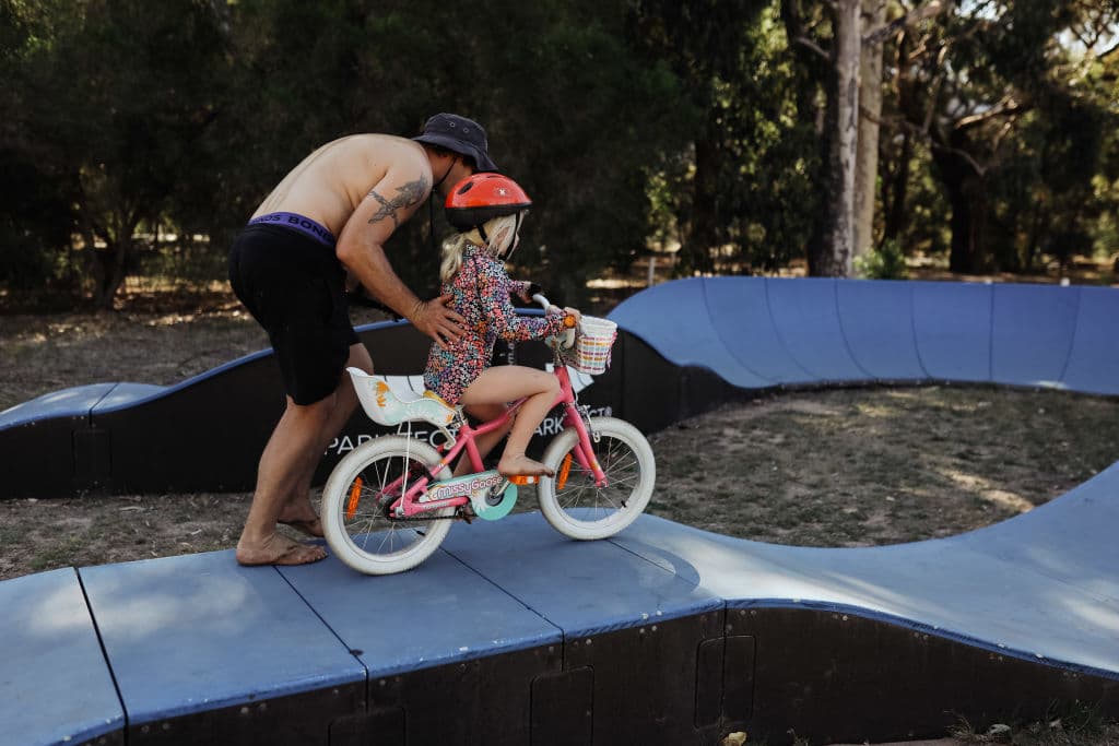 A dad and child ride a bike along a pump track.