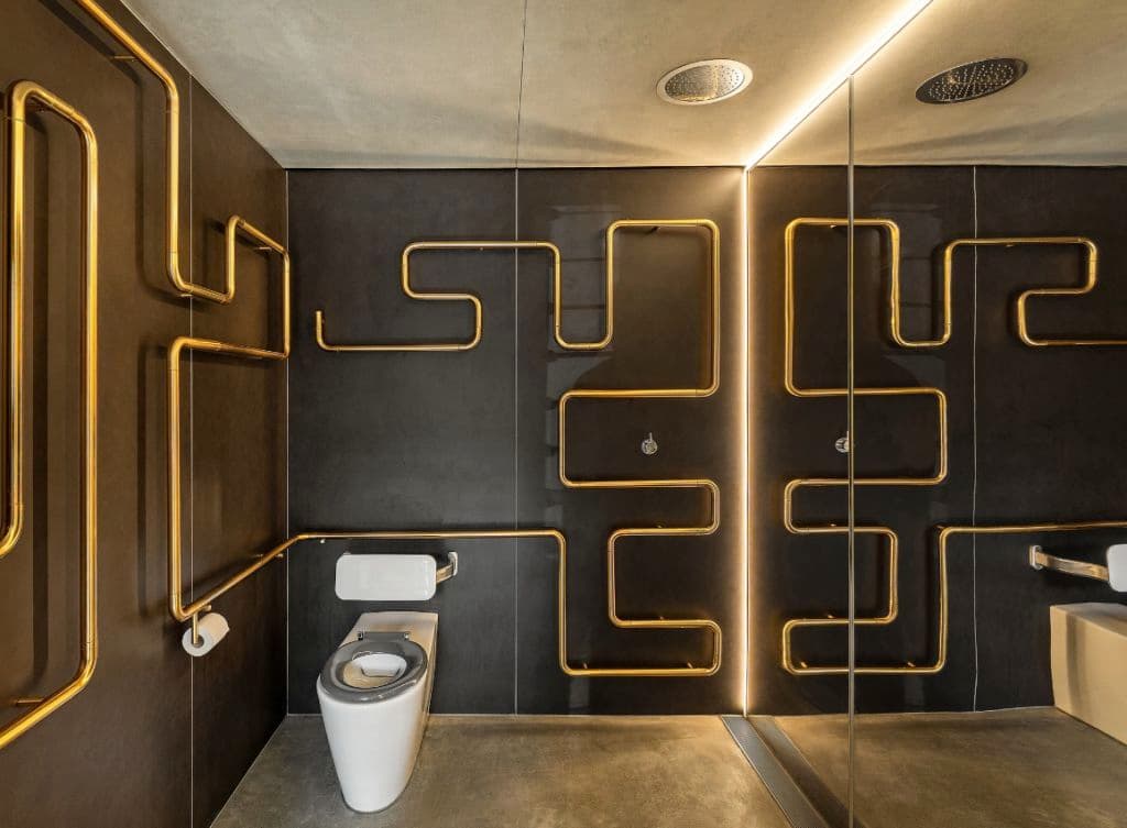 A toilet with black walls and copper-coloured pipes on the walls.