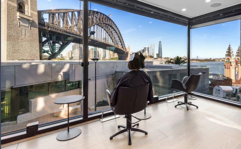 A woman with foils in her hair watches the Sydney Harbour Bridge view from inside a hair salon.