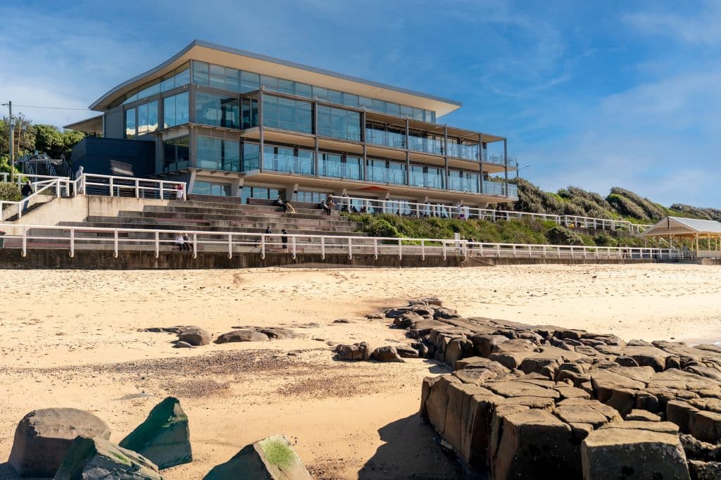 A modern tri-level building set on the sand overlooking a beach.