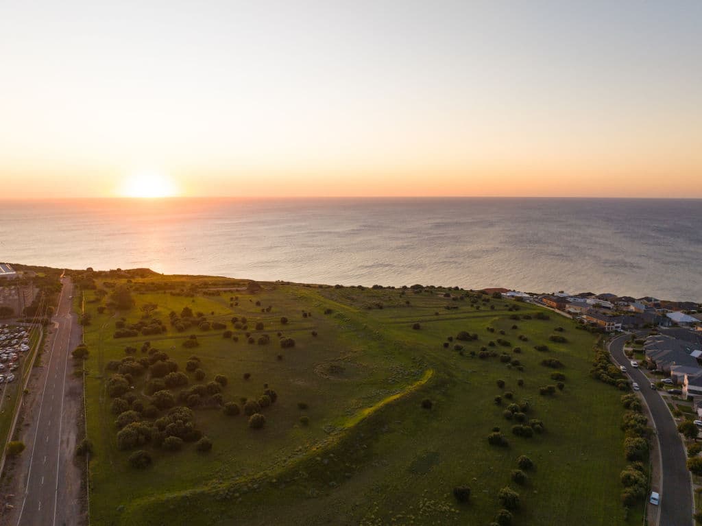 A warmly-lit sunset sits on the horizon line looking out to sea from Hallett Cove.