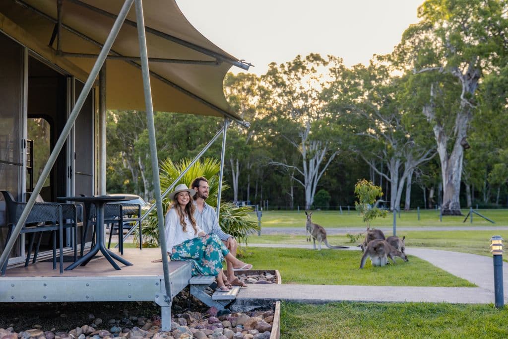 A man and woman sit on the steps at the edge of their glamping tent-style accommodation.