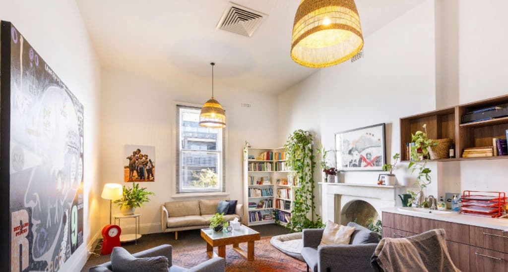 A room is well decorated with couches, paintings, rug and lampshades.