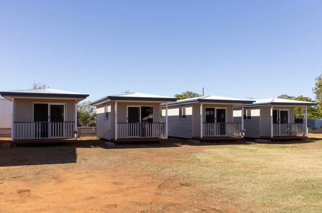 A row of cabins lined up on grass with a blue sky backdrop.