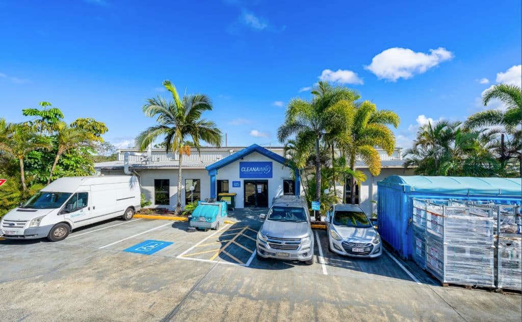 A single storey building is flanked with palm trees.