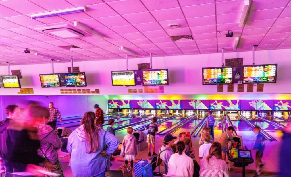 The inside of the bowling alley shows children and bowling lanes.