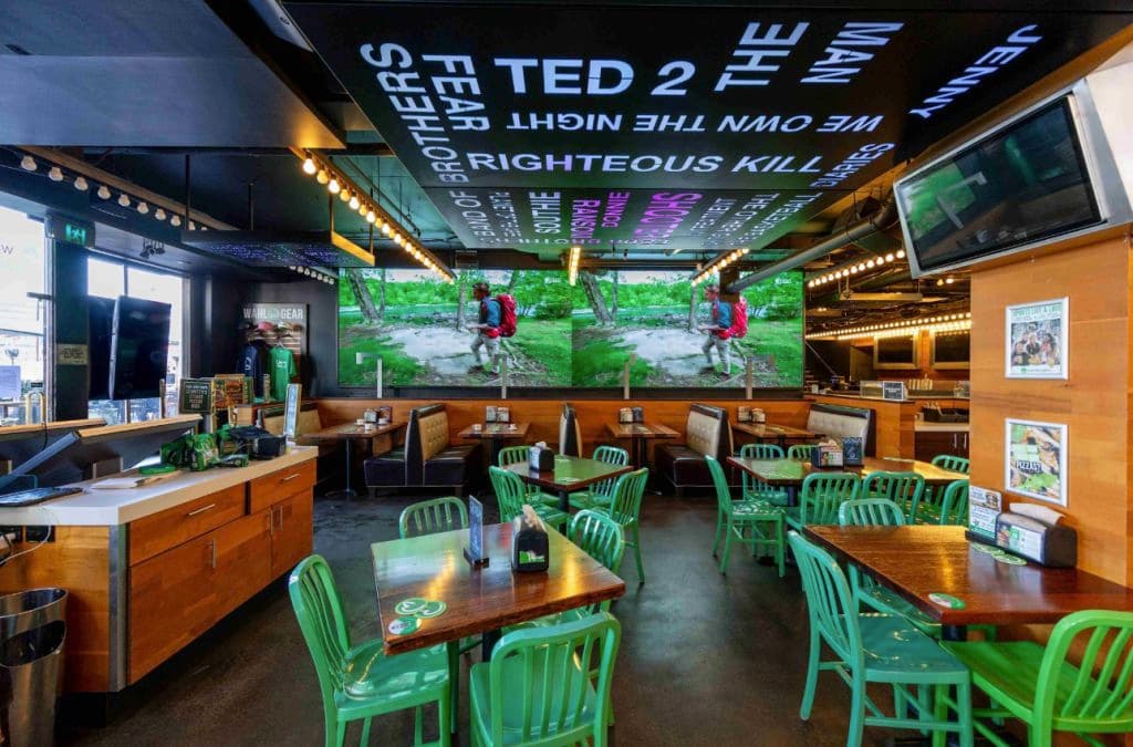 The former Wahlburgers restaurant fit out shows green chairs and dark interiors.
