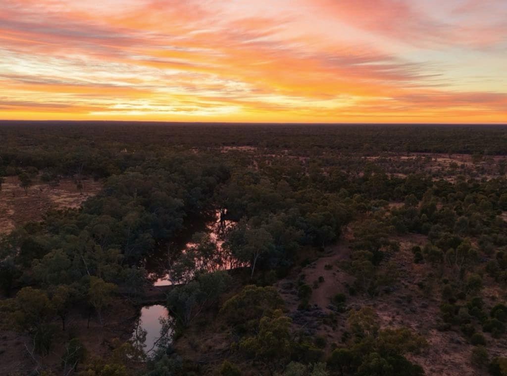An aerial shows a killer orange sunset and a water source on land.